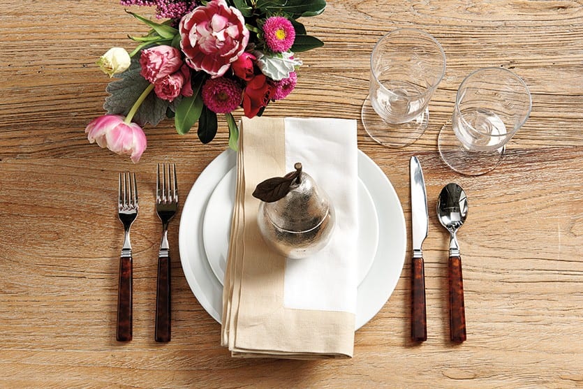 Table setting with pink flowers, neutral napkin, tortoise flatware, and wooden table