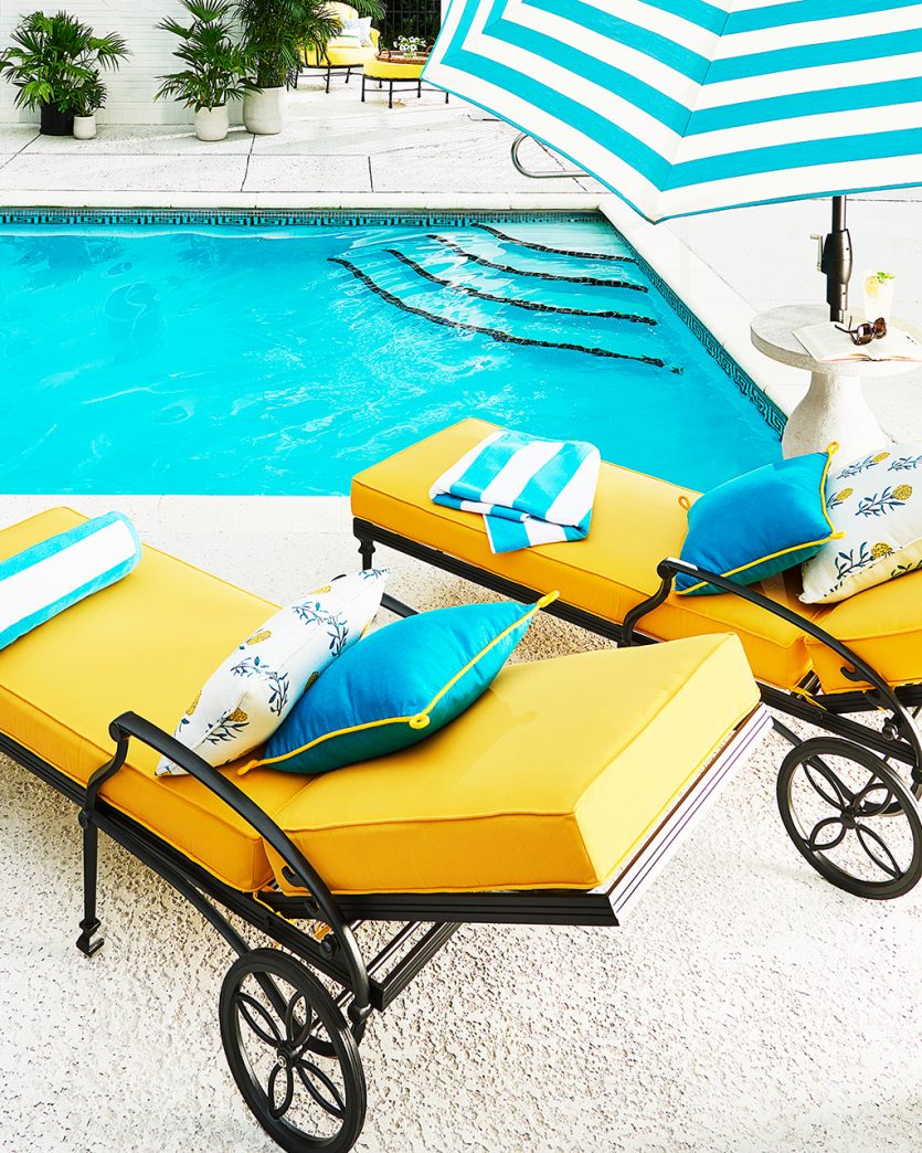 Yellow pool chaise with teal pillows and striped umbrella