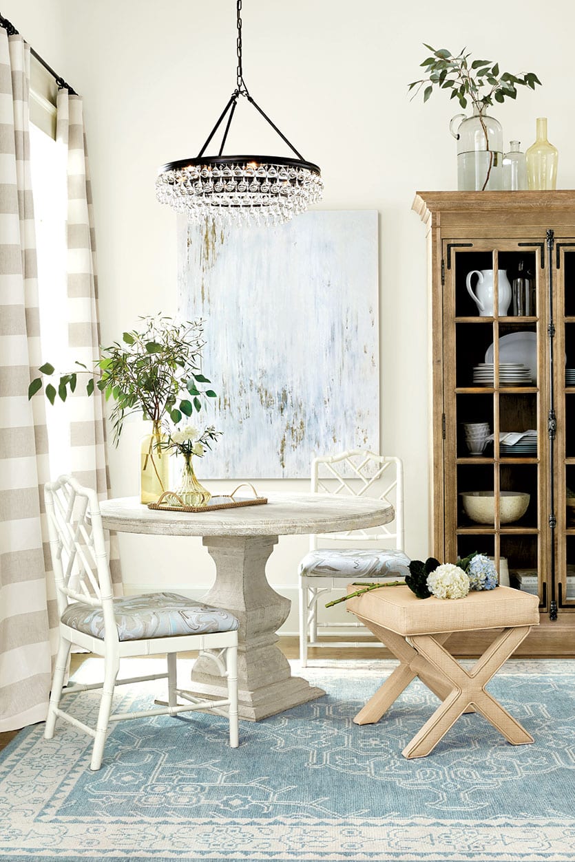 Sophisticated dining room with round table, crystal chandelier, marbleized fabric, and raffia x-bench