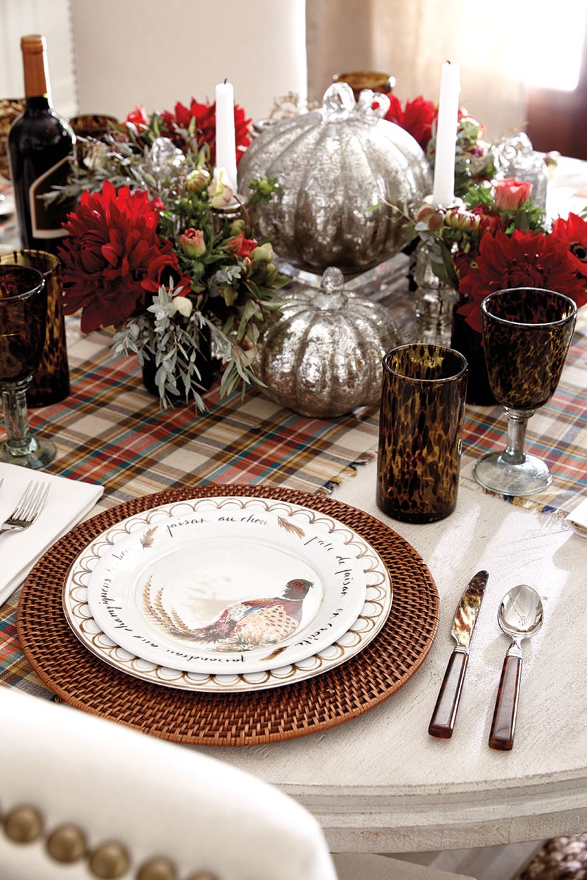 A Thanksgiving table with a plaid table runner, red flowers, and a pumpkin centerpiece