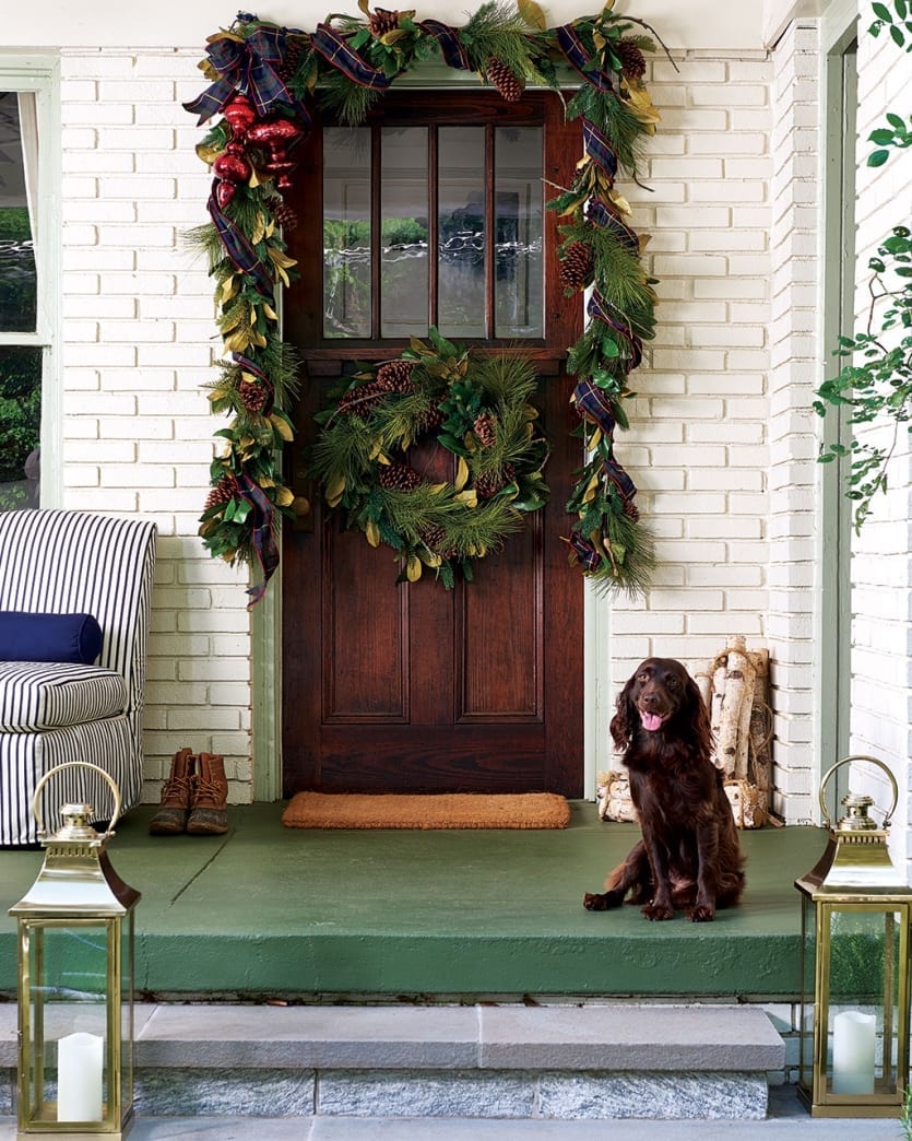 A white brick home with a wooden door, styled with Outdoor Christmas Decorations