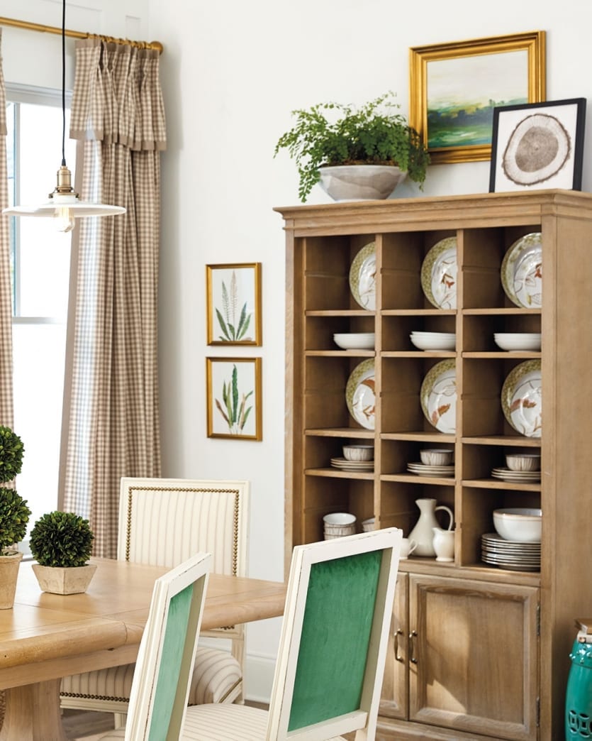 Dining room with green banquette, green and tan striped dining chairs, and tall oak cabinet storing coordinating dinnerware