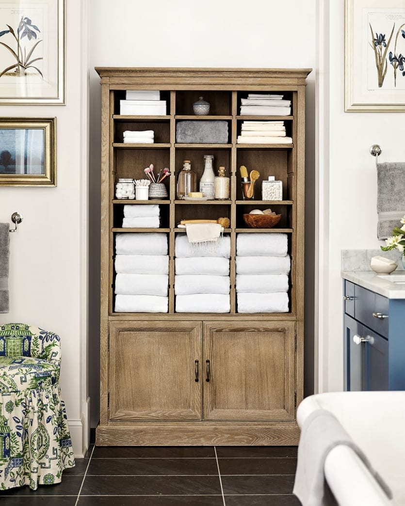 Ballard Designs oak Beckett cabinet used in a master bathroom with fluffy towels, bed linens, and toiletries