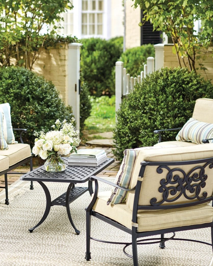 Neutral patio furniture with lush greenery around the perimeter