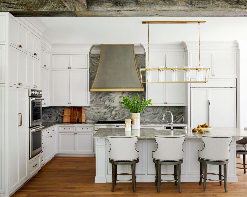 White kitchen designed by Amy Vermillion Interiors with upholstered barstools and marble backsplash