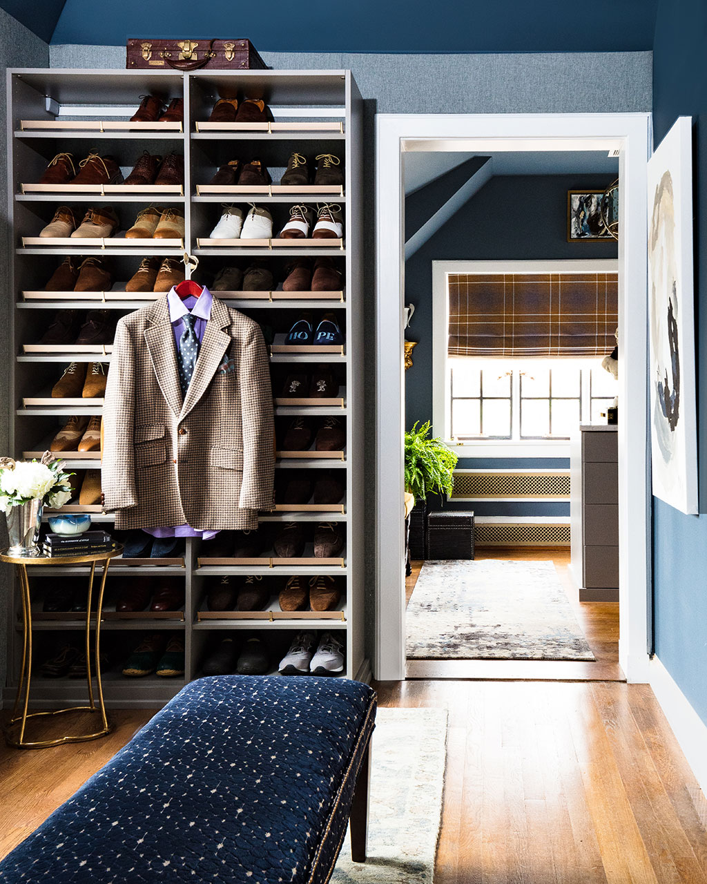 Men's closet with custom shoe shelves an upholstered bench and dark navy walls