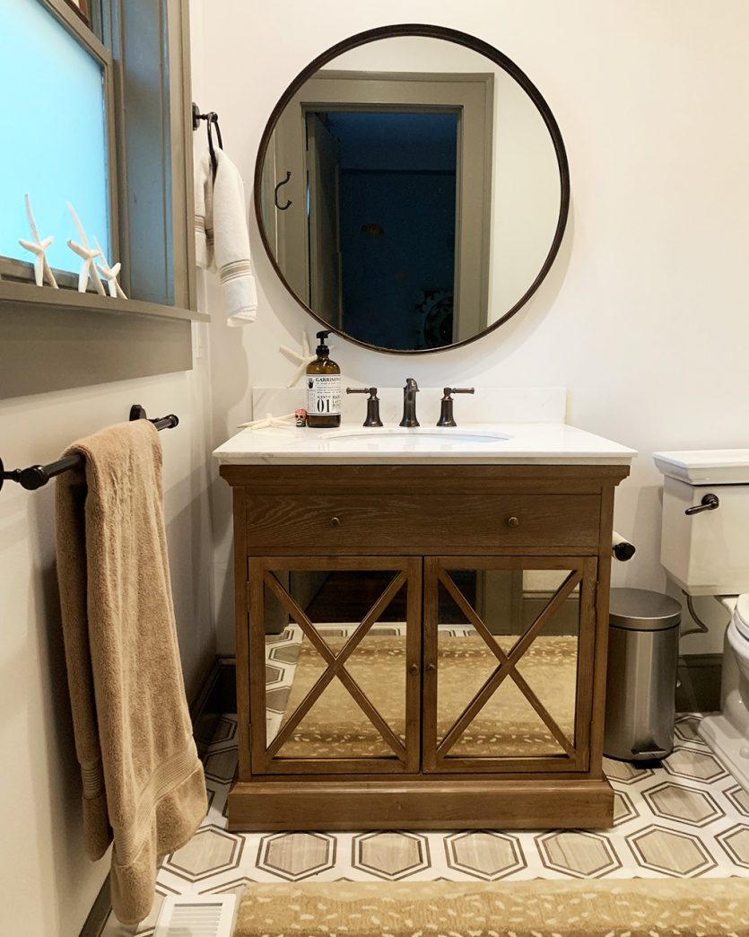 Guest bathroom with funky tile floors, belgian oak vanity, and large round mirror