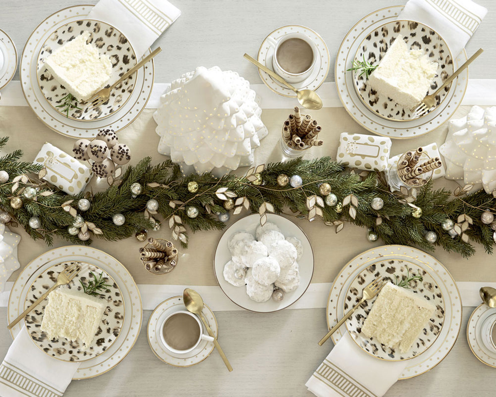 Faux greenery down the center of a Christmas table with ornaments and candles