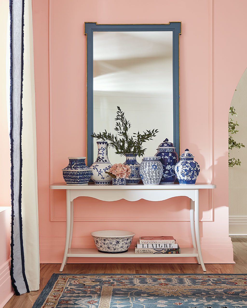 Corner of a living room with a bold pink wall color against blue decor; from Ballard Designs